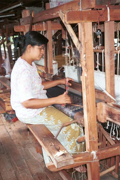 Jpeg 46K 980930E A three colour ikat being woven on a loom in the weaving mill at Innbawkon (Inpawkhon) on Lake Inle, Shan State. Note the weaver pulling on a cord to activate the 'flying shuttle' which has been added to the traditional Burmese frame loom to speed up the weaving process.