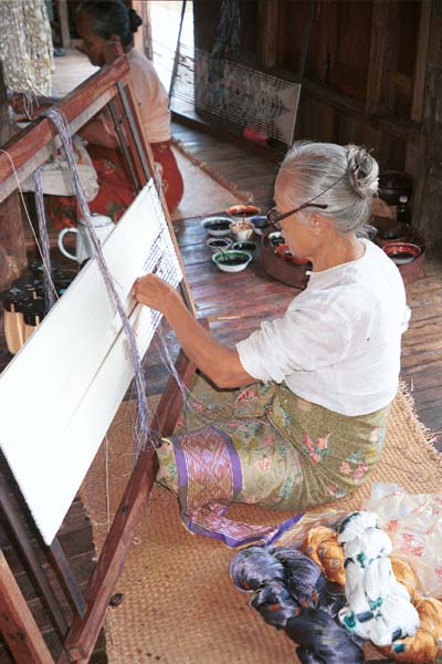 Jpeg 44K 9809O34 A woman tying the resists in the silk before the first application of dyeing in the ikat process at a weaving mill at Innbawkon (Inpawkhon) on Lake Inle, Shan State. Note that she has a sample strip of woven ikat over her lap which she is using as a pattern for the tying. In the foreground are some skeins of silk which have been tied.