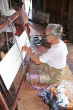 to Jpeg 44K 9809O34 A woman tying the resists in the silk before the first application of dyeing in the ikat process at a weaving mill at Innbawkon (Inpawkhon) on Lake Inle, Shan State. Note that she has a sample strip of woven ikat over her lap which she is using as a pattern for the tying. In the foreground are some skeins of silk which have been tied.