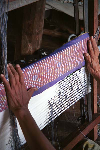 Jpeg 42K 9809O35 A woman checking her tying of the resists around the silk weft threads against a woven ikat strip which she is using as a pattern during tying before the first application of dye in the ikat process at a weaving mill at Innbawkon (Inpawkhon) on Lake Inle, Shan State.