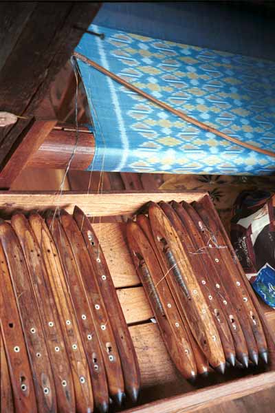 Jpeg 34K 9809P05 In the background three colour silk ikat on the loom and in the foreground the weft thread shuttles carefully in order ready to create the ikat pattern. All at a weaving mill at Innbawkon (Inpawkhon) on Lake Inle, Shan State. Note the 'bow' across the width of the weft to keep the width and tension constant.