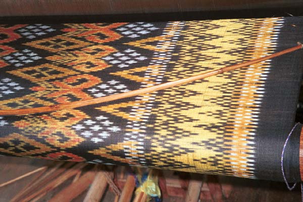 Jpeg 52K 9809P08A Four colour silk ikat on the loom at a weaving mill at Innbawkon (Inpawkhon) on Lake Inle, Shan State. Note the 'bow' across the width of the weft to keep the width and tension constant.