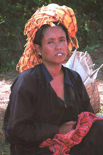 27 K Jpeg 9809H15 Pa'O woman sitting by her produce in Kalaw Market, Shan State. Note her turban tied from a woven scarf bought in the market and her Shan bag in her lap. She is wearing a short jacket, with long sleeves over her shift blouse which has a trim of embroidery in the 'V' of the neck and it is possible to see an echoing embroidery in the side seam of her blouse to the left of the photograph. The jacket has machine stitched detail around the piecing.