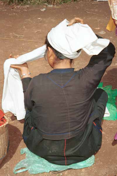 22K Jpeg 9809I24 Pa'O market trader in Kalaw 5-day rotating market re-tying her head covering - a length of white cotton cloth. Note the cut of her jacket over her loose blouse over her longyi.