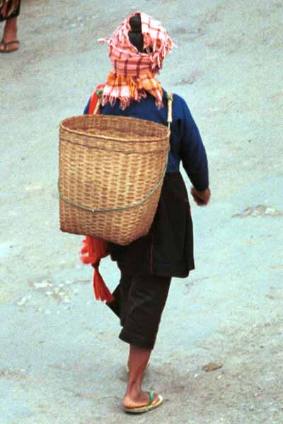 Jpeg 23K 9809J07 Pa'O woman at Kalaw Market, Shan State showing her short jacket over her lose blouse with coloured stitch detail down the back seam. The blouse is worn over a calf length plain longyiNote her woven (from the market) head scarf and Shan bag over her shoulder. Baskets similar to the one on her back were being sold by a Pa'O woman who had carried them into the market balanced on her head.