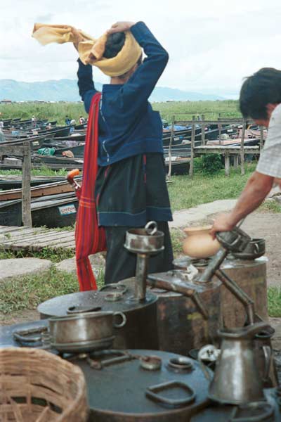 33K Jpeg 9809O11  Pa'O woman at Nampan 5-day rotating market, Lake Inle, Shan State. She is waiting whilst her liquid fuel is poured out. Note the short serge jacket with details of the fabric woven in the selvedge used to trim the back seam. She is wearing the jacket over her loose blouse with embroidered seam trimmings. This is then worn over a longyis.