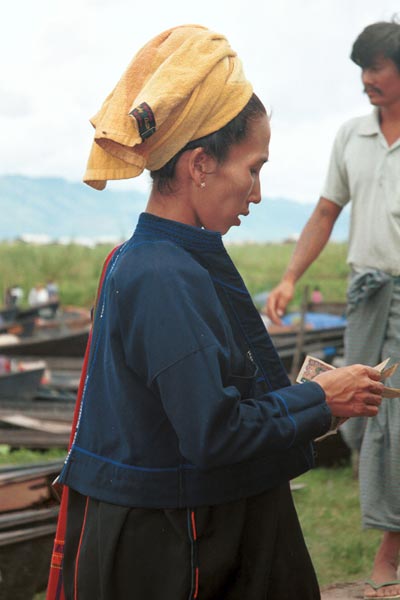 30K Jpeg 9809O12 Pa'O woman at Nampan 5-day rotating market, Lake Inle, Shan State. She is paying for her liquid fuel. Note the short serge jacket with details of the fabric woven in the selvedge used to trim the back seam and the edge of the front pocket. She is wearing the jacket over her loose blouse with embroidered seam trimmings. This is then worn over a longyis.