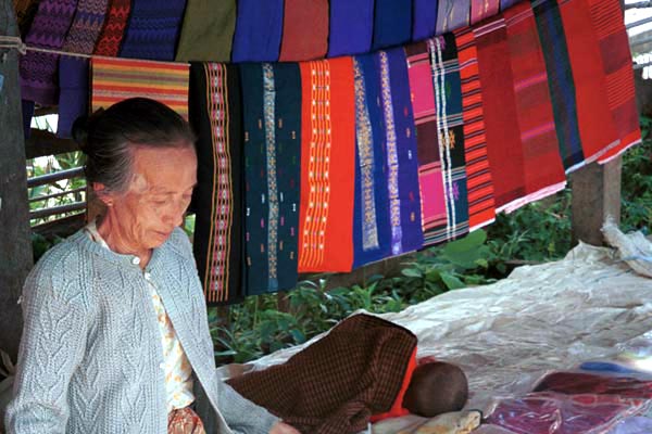 Jpeg 55K Woman selling woven textiles in Kalaw 5 day rotating market, Shan State. There would appear to be some Silver Palaung woven striped tubeskirts hanging to the right of the photo.