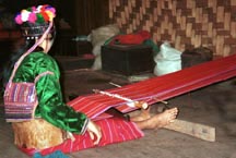 to 73K Jpeg Silver Palaung woman in Pein Ne Bin village, near Kalaw in southwestern Shan State, weaving a length of cotton fabric to make a tube skirt similar to the one she is wearing. Note the narrow stripes in warp threads. She is using a very simple backstrap loom with a wide leather back support. She is wearing a velvet decorated cap which is reputed to be worn by young girls and unmarried women although she appeared to be a married woman with a husband and baby. She has a very wide band of decoration using many rows of sequins on the back of her blouse.