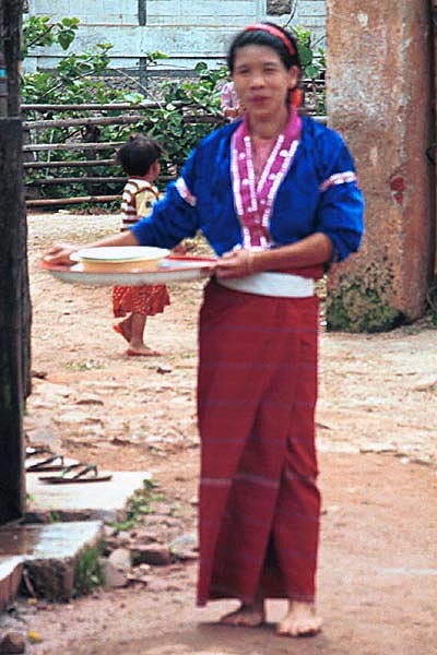 75K Jpeg Silver Palaung woman wearing the traditional hand woven tube skirt and decorated blouse carrying food utensils back from the communal meal for the 'Full Moon day' festival