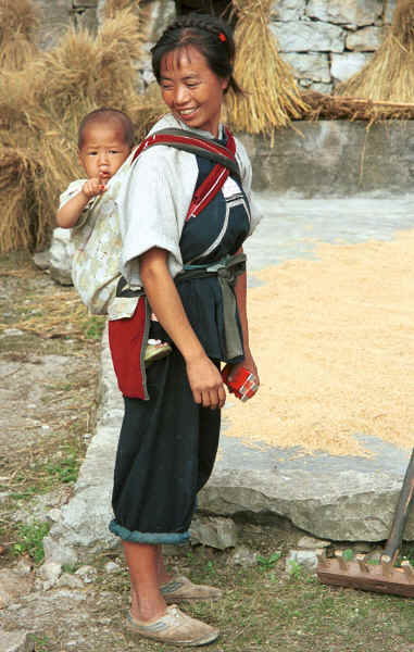 Bouyei mother and child pausing in raking the rice outside their home - Bi Ke village, Mi Gu township, Zhenfeng county, Guizhou province 0010r29.jpg