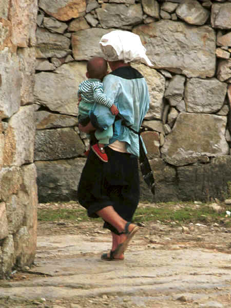 Bouyei woman and baby walking through the village showing the original dry stone walling of the houses - Bi Ke village, Mi Gu township, Zhenfeng county, Guizhou province 0010s13.jpg