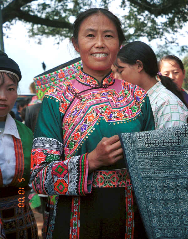 Batik artist shows her beautifully executed batik skirt length which indicates by its two intensities of indigo dye that it has been waxed twice.  I bought this length for my collection with the help of the school girl on the left who helped us barter by writing and interpreting the figures for the older lady.  Note the embroidered sleeves which can be removed and are placed over the sleeve of the jacket.  Da Shu Jia village, Xin Zhou township, Longlin county, Guangxi province 0010i18.jpg