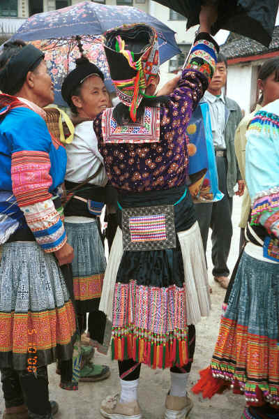 White Miao woman putting up her umbrella watched by Red Hat Miao women - De Wo market, De Wo township, Longlin county, Guangxi province 0010g04.jpg