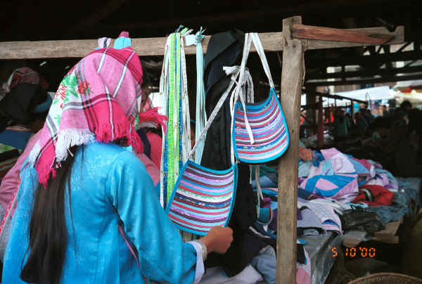 Side comb Miao woman looking at back aprons which, aside from their decorative appearance act as a protective pad underneath a bottom of a carrying basket - De Wo market, De Wo township, Longlin county, Guangxi province 0010g27.jpg