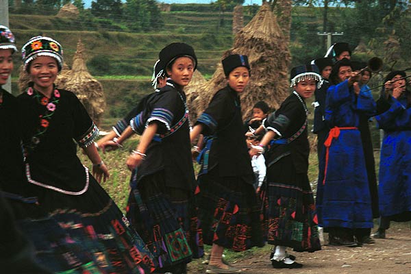 Jpeg 50K  0110D17  Girls dancing and trumpeters playing as part of our welcome to Gan He village, Ya Rong township, Huishui county, Guizhou province, south-west China. The people living in this village are known as Qing Miao. There has been much intermarriage between Miao and Bouyei which is evident from the every-day costume of the women. The pieced skirts of applique and wax-resist being worn by the girls were originally only worn at funerals but today they are worn for special festivals and dance competitions.