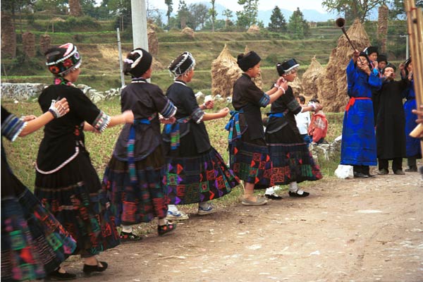 Jpeg 57K  0110D18A Girls dancing as part of our welcome to Gan He village, Ya Rong township, Huishui county, Guizhou province, south-west China. The people living in this village are known as Qing Miao. There has been much intermarriage between Miao and Bouyei which is evident from the every-day costume of the women. The pieced skirts of applique and wax-resist being worn by the girls were originally only worn at funerals but today they are worn for special festivals and dance competitions.