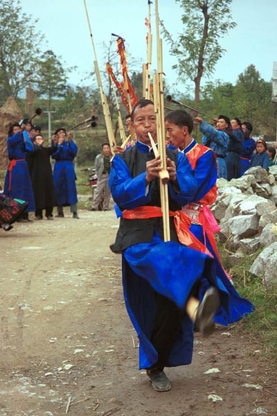 Jpeg 55K 0110D20  Villagers welcoming us to Gan He village, Ya Rong township, Huishui county, Guizhou province, south-west China. Musicians led by men playing on large lusheng pipes and followed by men blowing on very long (and loud) trumpets. The people living in this village are known as Qing Miao. There has been much intermarriage between Miao and Bouyei which is evident from the costume of the women. 