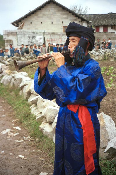 Jpeg 55K 0110D21  Trumpeter blowing his welcome to Gan He village, Ya Rong township, Huishui county, Guizhou province, south-west China. Note the complex weaving of the ends of his head-cloth. The people living in this village are known as Qing Miao. There has been much intermarriage between Miao and Bouyei which is evident from the costume of the women.