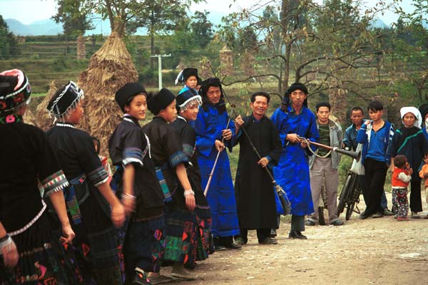 Jpeg 54K  0110D24 Girls dancing past the trumpeters as part of our welcome to Gan He village, Ya Rong township, Huishui county, Guizhou province, south-west China. The people living in this village are known as Qing Miao. There has been much intermarriage between Miao and Bouyei which is evident from the every-day costume of the women. The pieced skirts of applique and wax-resist being worn by the girls were originally only worn at funerals but today they are worn for special festivals and dance competitions.