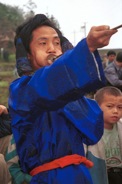 Jpeg 51K  0110D29 Trumpeter blowing his welcome at Gan He village, Ya Rong township, Huishui county, Guizhou province, south-west China. Note the complex weaving of the ends of the head-cloth. These long trumpets are very loud! The people living in this village are known as Qing Miao.