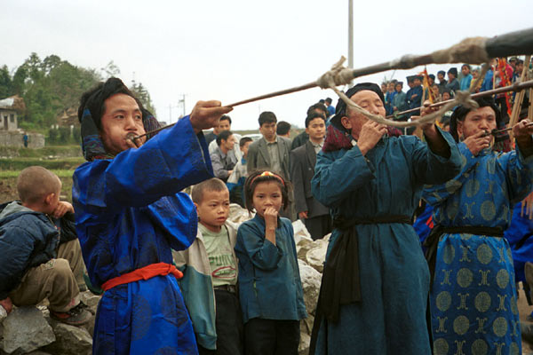 Jpeg 58K  0110D30 Trumpeters blowing their welcome at Gan He village, Ya Rong township, Huishui county, Guizhou province, south-west China. Note the complex weaving of the ends of the head-cloths.These long trumpets are very loud! The people living in this village are known as Qing Miao. 