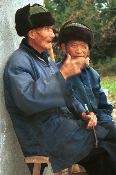 Jpeg 56K  0110D32 Two old men watching our welcome to Gan He village, Ya Rong township, Huishui county, Guizhou province, south-west China. The people living in this village are known as Qing Miao.