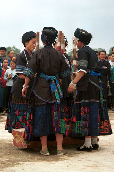 Jpeg 56K  0110D33 Women beating sticky rice as part of a dance programme in Gan He village, Ya Rong township, Huishui county, Guizhou province, south-west China. The people living in this village are known as Qing Miao. There has been much intermarriage between Miao and Bouyei which is evident from the every-day costume of the women. The pieced skirts of applique and wax-resist being worn by the girls were originally only worn at funerals but today they are worn for special festivals and dance competitions. Note the bands of complex weaving on the sleeves of the women's jackets.