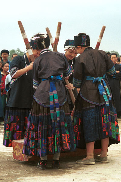 Jpeg 57K 0110D34 Women beating sticky rice as part of a dance programme in Gan He village, Ya Rong township, Huishui county, Guizhou province, south-west China. The people living in this village are known as Qing Miao. There has been much intermarriage between Miao and Bouyei which is evident from the every-day costume of the women. The pieced skirts of applique and wax-resist being worn by the girls were originally only worn at funerals but today they are worn for special festivals and dance competitions. Note the bands of complex weaving on the sleeves of the women's jackets.