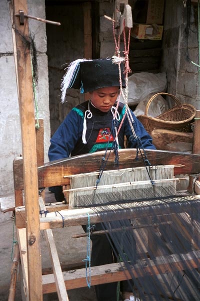 Jpeg 55K  0110E07   Woman weaving an indigo plaid fabric on an upright heddle loom in Gan He village, Ya Rong township, Huishui county, Guizhou province, south-west China. The people living in this village are known as Qing Miao. There has been considerable intermarriage between Miao and Bouyei and the costume is very mixed.