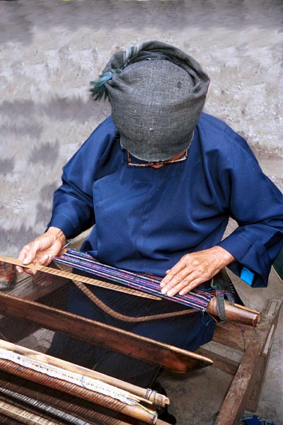 Jpeg 53K 0110E08  Woman working on some complex weaving on a backstrap loom in Gan He village, Ya Rong township, Huishui county, Guizhou province, south-west China. The weaving will be cut into pieces to insert into the sleeves of women's jackets and to use on the ornamental ends of men's head-cloths. The people living in this village are known as Qing Miao. There has been considerable intermarriage between Miao and Bouyei and the costume is very mixed. 