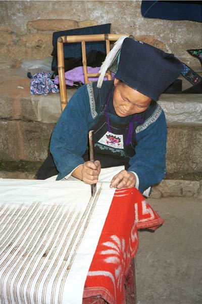 Jpeg 48K 0110E21  A woman applying wax resist to cotton cloth in Gan He village, Ya Rong township, Huishui county, Guizhou province. This is a Qing Miao (or Bouyei/Miao as there has been much intermarriage and the costume is very mixed).