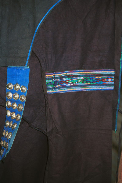 Jpeg 55K  0110E23  Part of a woman's indigo jacket showing an inserted band of weaving in the sleeve and silver buttons on the fastening in Gan He village, Ya Rong township, Huishui county, Guizhou province. This is a Qing Miao (or Bouyei/Miao as there has been much intermarriage and the costume is very mixed). 