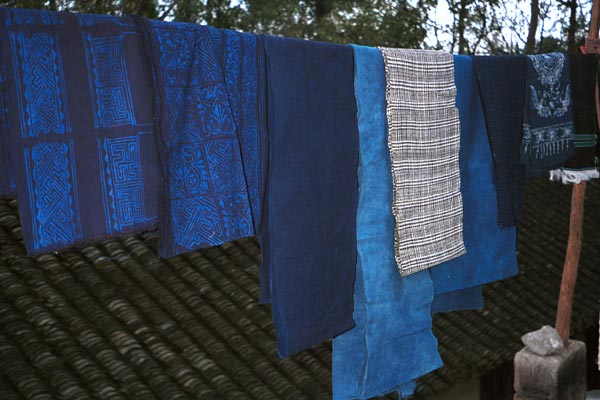 Jpeg 49K  0110E24Various fabrics hanging on display - wax resist in two shades of indigo, plain fabric in different indigo shades and a length of plaid weaving in Gan He village, Ya Rong township, Huishui county, Guizhou province. This is a Qing Miao (or Bouyei/Miao as there has been much intermarriage and the costume is very mixed). 