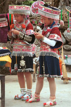 to Jpeg 176 Two Iron beating Miao women in Gao Zhai village, Bai Jin township, Huishui county, Guizhou province working on some embroidery and showing off their festival costume against a back drop of an even brighter hat and two of their jackets 0110C09