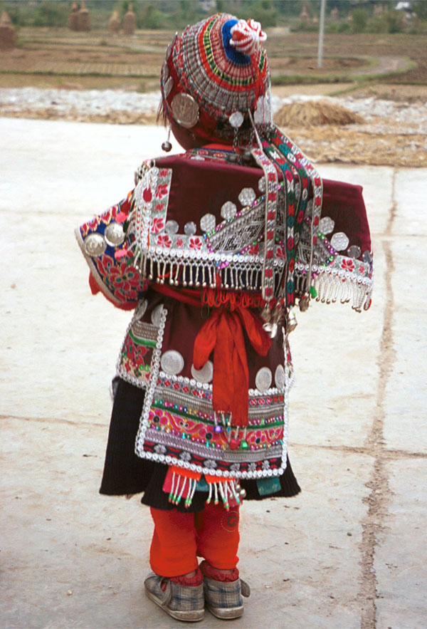 Jpeg 142K Iron beating Miao festival costume in miniature worn by one of little girls who danced for us in Gao Zhai village, Bai Jin township, Huishui county, Guizhou province. She is wearing what looks like a very ornate baby carrier on her back. Note the finely gathered hat crown worn by the little girl and shown in closeup in photos further down in the photo gallery. I bought one of these beautifully made hats for my collection 0110C14