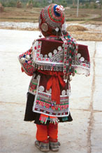 to Jpeg 142K Iron beating Miao festival costume in miniature worn by one of little girls who danced for us in Gao Zhai village, Bai Jin township, Huishui county, Guizhou province. She is wearing what looks like a very ornate baby carrier on her back. Note the finely gathered hat crown worn by the little girl and shown in closeup in photos further down in the photo gallery. I bought one of these beautifully made hats for my collection 0110C14