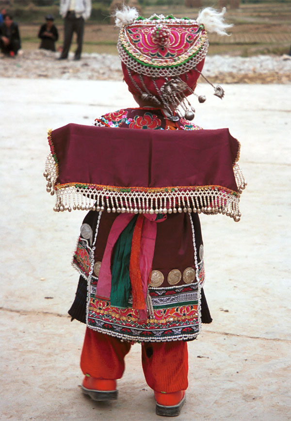 Jpeg 129K Iron beating Miao festival costume in miniature worn by one of little girls who danced for us in Gao Zhai village, Bai Jin township, Huishui county, Guizhou province. She is wearing what looks like a very ornate baby carrier on her back 0110C15