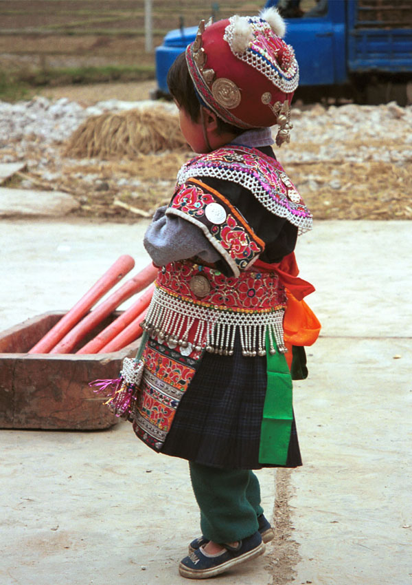 Jpeg 139K Iron beating Miao festival costume in miniature worn by one of little girls who danced for us in Gao Zhai village, Bai Jin township, Huishui county, Guizhou province. Her costume is finely made. Note the beautifully woven and subtle woven striped indigo skirt that she is wearing which is a perfect miniature version of the adult woman's skirt 0110C16