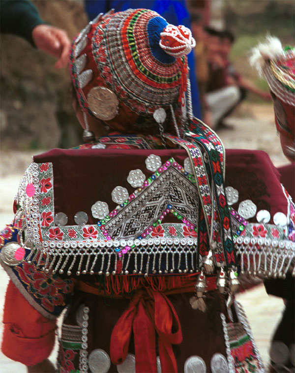 Jpeg 141K Iron beating Miao festival costume in miniature worn by one of little girls who danced for us in Gao Zhai village, Bai Jin township, Huishui county, Guizhou province. She is wearing what looks like a very ornate baby carrier on her back. Note the finely gathered hat crown worn by the little girl and shown in closeup in photos further down in the photo gallery. I bought one of these beautifully made hats for my collection 0110C23