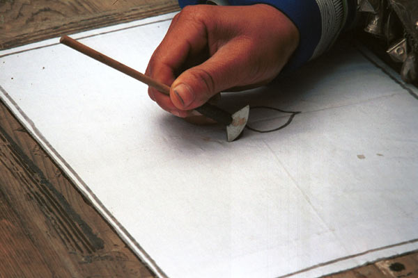 Jpeg 36K 0111F35 Gejia woman starting a wax resist design. Note that she has fixed her cotton fabric to her waxing board by making outlines of wax around the edge of the fabric which then dries fixed onto the board. Ma Tang village, Kaili City, Guizhou province.