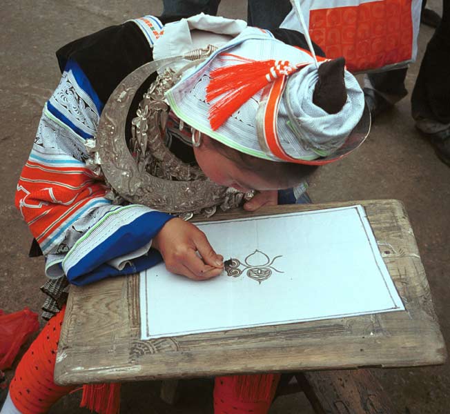 Jpeg 59K 0111G01 Gejia woman in full festival finery demonstrating wax resist. The fabric on her own costume is commercially printed with traditional Gejia designs and not waxed. Ma Tang village, Kaili City, Guizhou province.