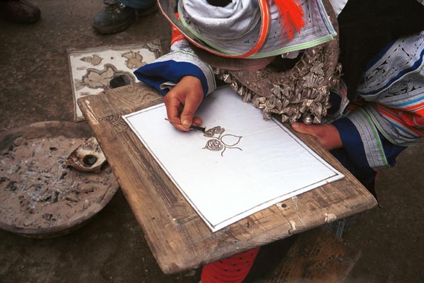 Jpeg 49K 0111G04 Gejia woman in full festival finery demonstating wax resist. Ironically all the apparently waxed material on her costum machine-made commercial fabric based on traditional Gejia wax resist designs. Ma Tang village, Kaili City, Guizhou province.