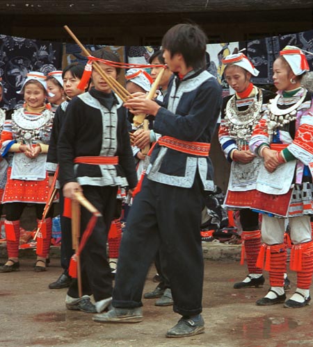 Jpeg 58K 0111G07 Boys in Gejia dance troupe performing on lusheng pipes in Ma Tang village, Kaili City, Guizhou province in November 2001. The apparently wax resist fabric in their costumes - at least the headdress, apron and sleeves of the blouse of the women - are now generally made from commercially printed fabric which imitates the Gejia traditional wax resist designs. 