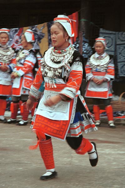 Jpeg 52K 0111G18 Gejia dance troupe performing in Ma Tang village, Kaili City, Guizhou province in November 2001. The apparently wax resist fabric in their costume - at least the headdress, apron and sleeves of the blouse - are now generally made from commercially printed fabric which imitates the Gejia traditional wax resist designs