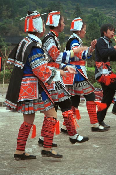 Jpeg 56K 0111G20 Gejia dance troupe performing in Ma Tang village, Kaili City, Guizhou province in November 2001. The apparently wax resist fabric in their costume - at least the headdress, apron and sleeves of the blouse - are now generally made from commercially printed fabric which imitates the Gejia traditional wax resist designs 