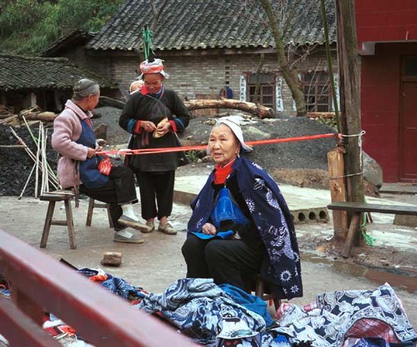 Jpeg 58K 0111G35 Gejia women weaving braids, knitting hairnets and sewing by a heap of wax resist clothing.  Ma Tang village, Kaili City, Guizhou province.