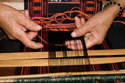 Jpg 103K - Weaver Huang Ji Xiang, who is a member of the Qi subgroup of the Li people, making the cloth that is called "Li brocade" locally. Weaving proceeds via two separate sheds. After adding a row of ground weft the weaver switches attention to the upper shed where the pattern is formed. She first selects the region of interest with the light colored wooden pick at the bottom of the photo, then uses a second pick to select the warps for the supplementary weft, which is then added by passing the thread from hand to hand because the distance is too short to need a spindle or shuttle. She then beats this down using the pick/sword and switches back to the lower shed ... and so the weaving goes.