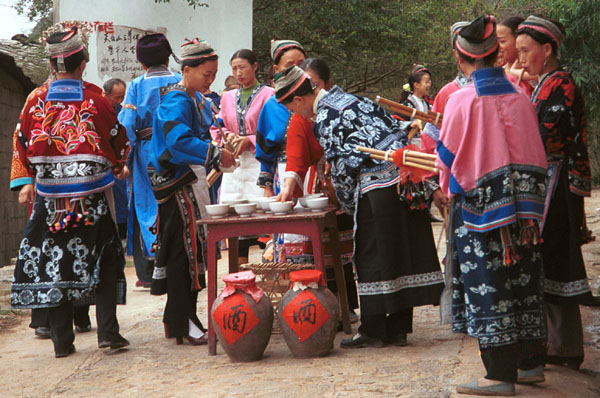 Jpeg 94K Miao women getting ready to greet with alchohol and lusheng pipes as we enter Lou Jia Zhuang village, Anshun city, Guizhou province. Note the flowers in the wax resist on their festival clothing which may be the reason that are sometimes called 'Flower Miao'. 0110A12