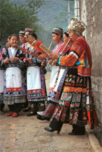 to Jpeg 123K Miao women playing lusheng pipes to welcome us. The two girls to the left are wearing the modern festival costume of the village and are holding carved charms on threads to put over out heads. The woman near to the camera on the right has a skirt and silver head dress which is not local to this area. It may have been adopted to create more of a stir in the dance competitions or she might have maried into the village from elsewhere. Lou Jia Zhuang village, Anshun city, Guizhou province. 0110A20